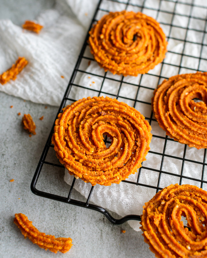 A plate of Chakli on a kitchen counter with natural lighting and some decorative elements in the background.