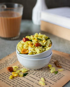 chivda playfully placed in a white bowl inside another white bowl with tea in a glass in the background